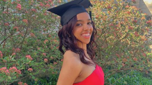 A portrait of Raygn乔丹 ’24 smiling and wearing a red dress and black graduation cap.